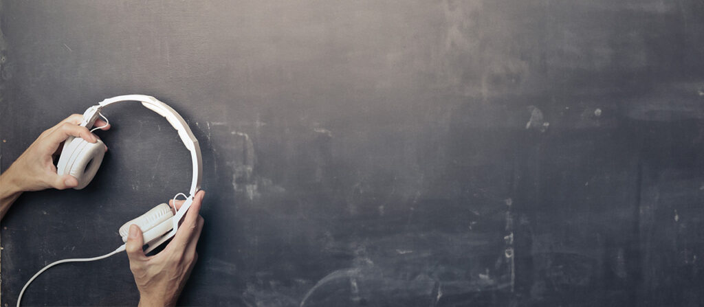 a pair of men's hands holding a white pair of headphones with a blackboard background.